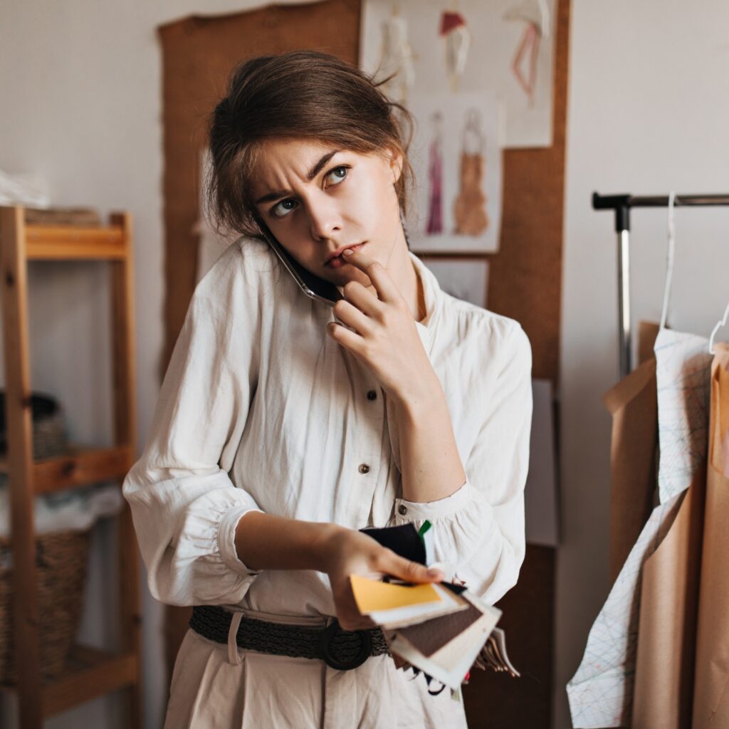 woman talking phone holding fabric samples thoughtfully posing