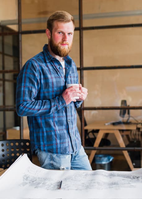 confident-man-holding-cup-coffee-standing-near-desk