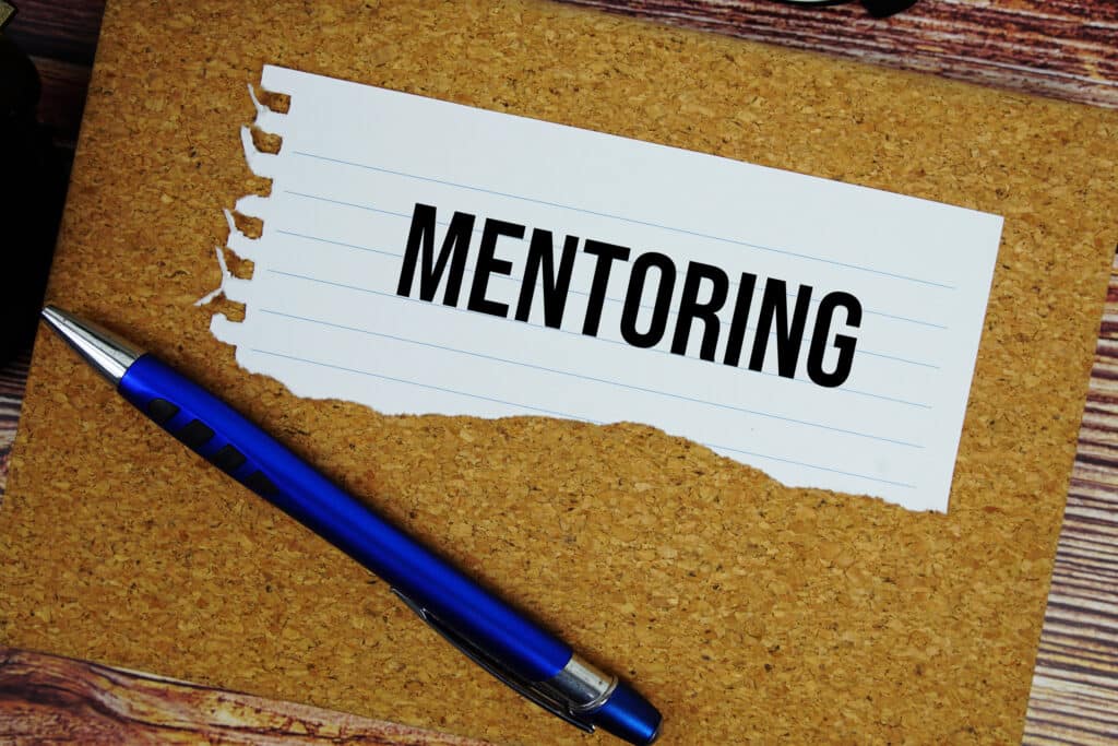 Mentoring text written on paper torn with pen top view on wooden background